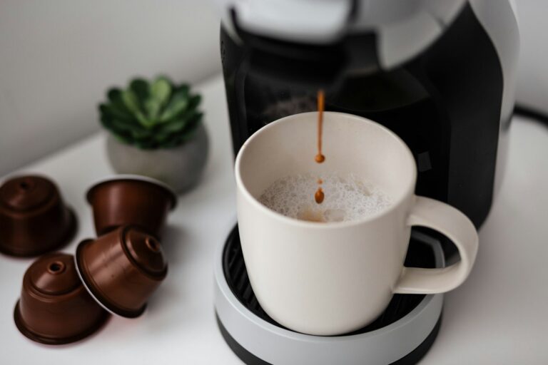 Kapselmaschine füllt Kaffee in einen weißen Becher, daneben liegen Kaffeekapseln