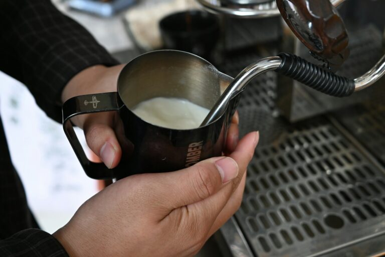 Milch wird in einem Milchkännchen aus Edelstahl mit der Dampfdüse aufgeschäumt